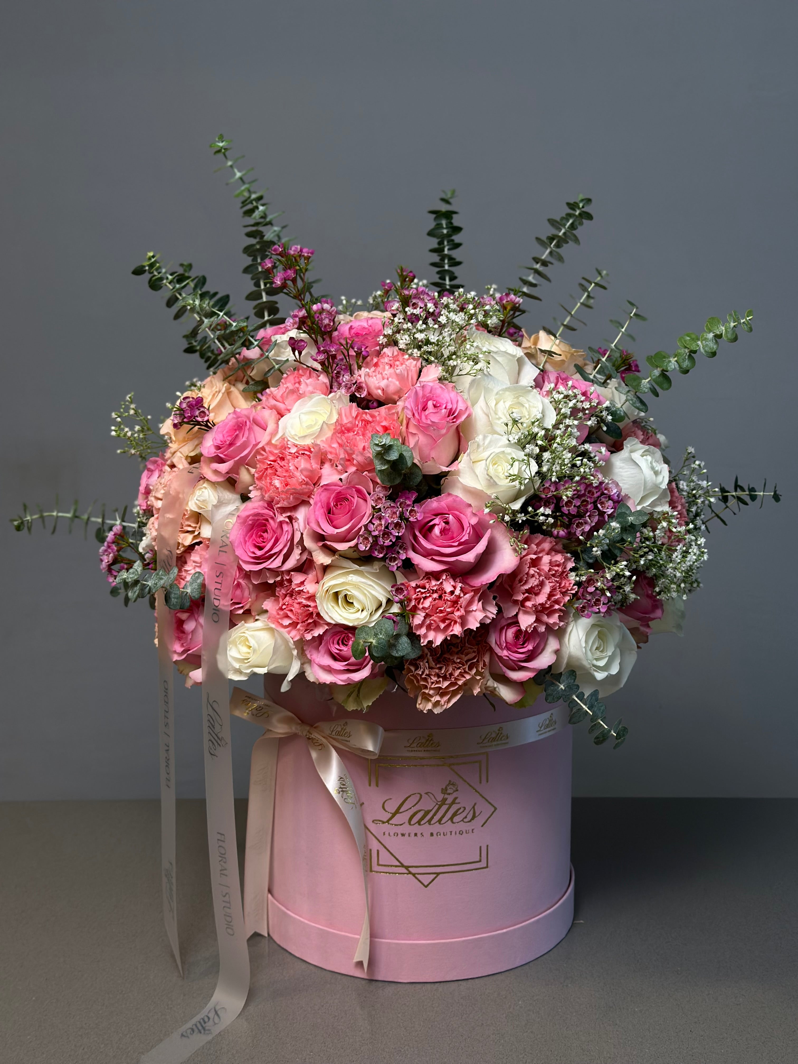 A luxurious floral arrangement featuring roses in shades of pink and white, carnations, waxflowers, and eucalyptus sprigs in a pink box